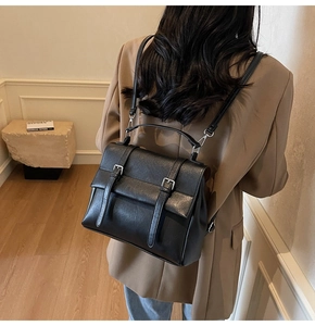 Rear view of model wearing a black matte leather backpack with silver metal buckles