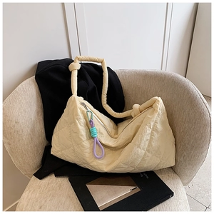 Detail of cream quilted tote bag featuring a thick knotted handle and colorful rope zipper pull