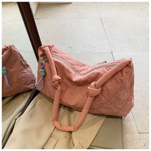 Detail of pink quilted tote bag featuring padded handles and a colorful braided tassel