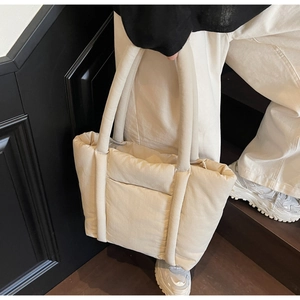Dettaglio di una borsa tote trapuntata beige con manici imbottiti e una tasca anteriore