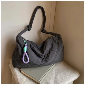 Detailed macro view of dark grey quilted puffer tote bag with decorative knot charm