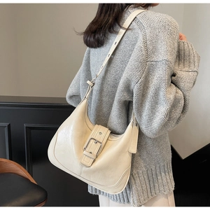 Detail einer beigen Schultertasche mit Lederstruktur und Schnalle auf grauem Pullover