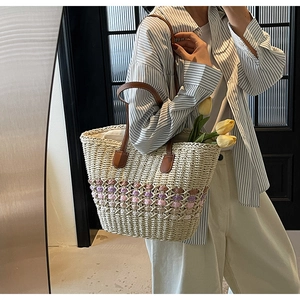 Detail of woven straw tote bag with brown leather straps and colorful pattern