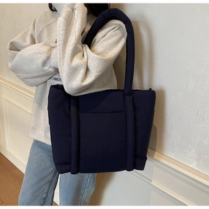 Borsa tote trapuntata blu scuro con spallacci imbottiti spessi mostrata su un modello