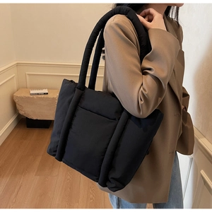 Dettaglio di una borsa tote trapuntata nera portata a spalla in un ambiente moderno