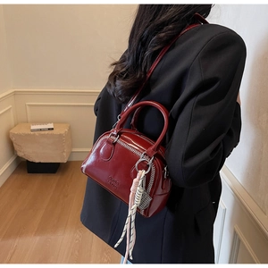 Detail of burgundy Boston bag with white stitching and woven pendant on model back