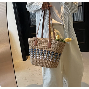 Detail of hand-woven straw tote with blue-purple accent and brown leather straps