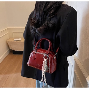 Detail of red glossy Boston bag with contrast white stitching and colorful tassel charm