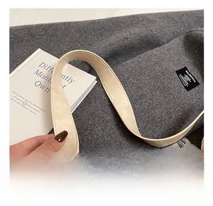 Detail shot of a soft cream leather tote bag handle placed on grey tweed fabric with books