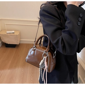 Detail of dark brown leather Boston bag featuring white contrast stitching and woven charm