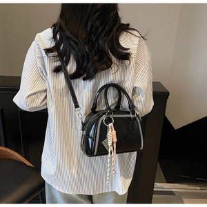 Detail of black Boston bag featuring white contrast stitching and trendy knot tassel charm