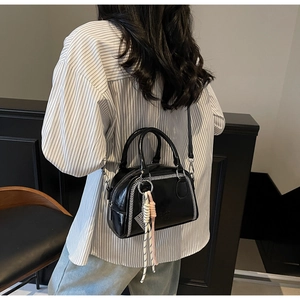 Detail of a black glossy Boston bag with white stitching and a woven rope charm