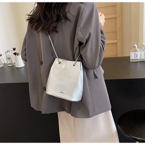 Detail shot of silver bucket bag with chain strap and metallic finish on shoulder