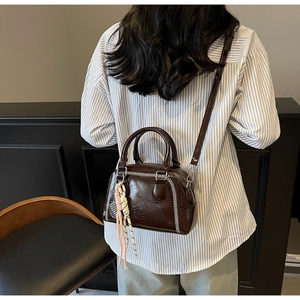 Detail of dark brown mini pillow bag with white baseball stitching and tassel charm