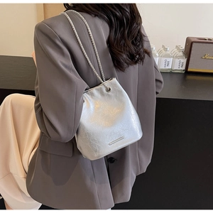 Detail of silver cracked leather bucket bag with chain strap worn by a female model