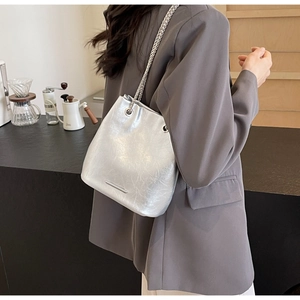 Close-up of a silver bucket bag with woven metal chain strap on woman's shoulder