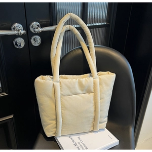 Dettaglio borsa tote trapuntata color crema con manici lunghi su sedia nera