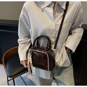 Close-up of brown leather pillow bag with white stitching and colorful woven charm