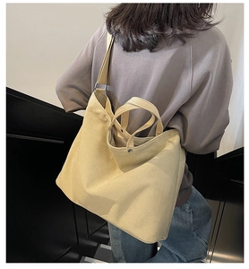 Detail of beige canvas tote bag with adjustable strap and metal hardware shown on model