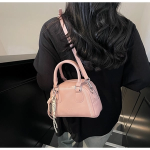 Detail view of pink pillow bag showing white stitching, logo, and braided charm strap