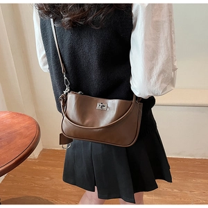 Brown vintage leather shoulder bag with silver buckle worn by a model in a warm room