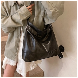 Detail shot of a large black oil wax leather tote bag with silver buckle on a model