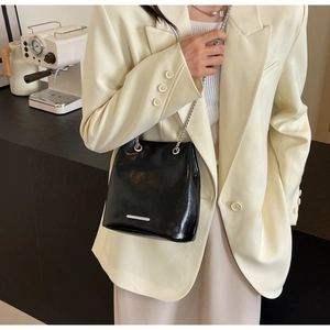 Detail of black glossy leather bucket bag with silver chain strap and metal buckle