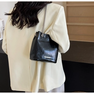 Detail of black drawstring bucket bag with silver chain strap and oily leather texture