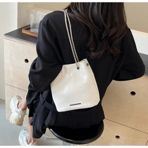 Detail of white bucket bag featuring dual silver chains and sleek metal trim on leather
