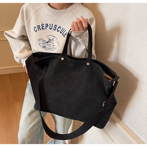 Detail of a large black canvas tote bag showing wide shoulder strap and spacious interior