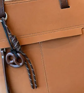 Macro detail of dark brown leather tote with contrast stitching and pretzel charm