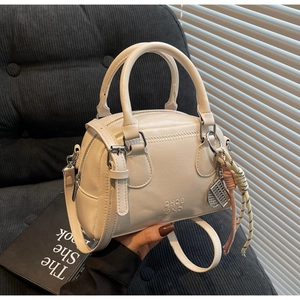 Close-up of cream Boston bag with leather texture, dual handles, and abacus charm detail