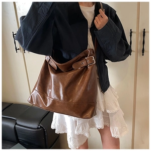 Close-up of vintage brown leather tote bag with metallic buckle detail and wide shoulder strap
