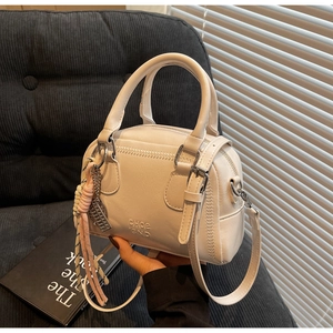 Close-up of white leather bowling bag with braided V-detail and fringe tassel accessory
