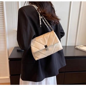 Detail of a beige quilted crossbody bag with V-shaped stitching and a silver chain strap
