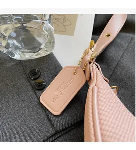 Detail of pink faux leather texture and branded tag on a crescent underarm bag