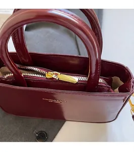 Detailopname van de gladde gouden rits en het logo op de wijnrode leren handtas
