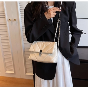 Detail of a beige quilted shoulder bag with silver square lock and chain strap on a model