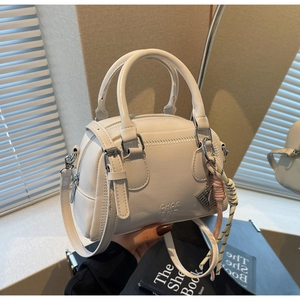 Detail of cream-colored bowling bag with top handles, logo embossing and woven rope pendant