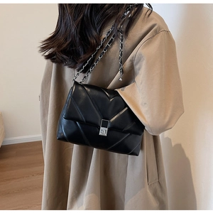 Detail of black quilted leather shoulder bag with silver chain strap on a model