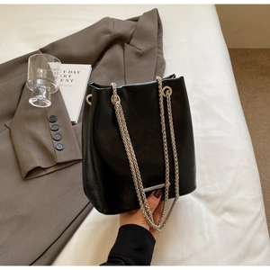 Detail of glossy black leather bucket bag with silver chain strap in an urban setting