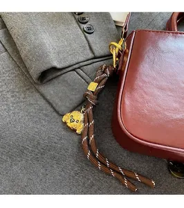 Detail van een bruine gevlochten sleutelhanger met gouden teddybeer aan een tas