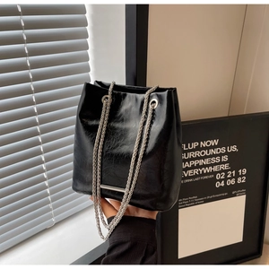 Detail of black glossy bucket bag with silver chain straps and soft crinkled leather texture