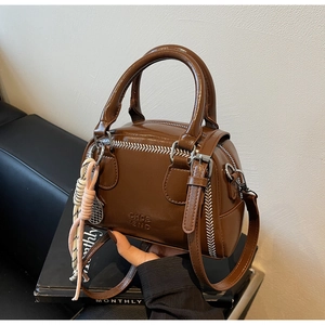 Detail of brown PU Boston bag showing contrast zigzag stitching and hanging rope charm