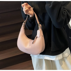 Detail of pink crescent bag with woven texture worn by model on a dark staircase