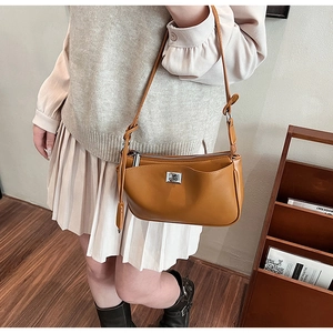 Detail of tan faux leather shoulder bag with silver logo worn in a cozy indoor setting