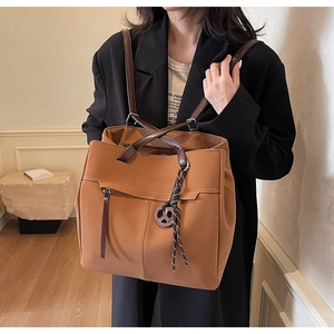 Detail of caramel leather tote bag with braided tassel charm and silver hardware accents