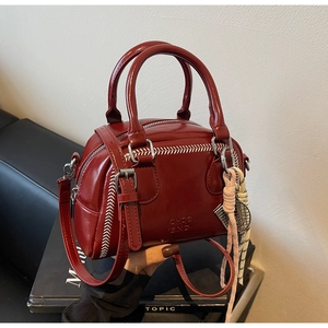 Macro shot of red glossy boston bag with white stitching and decorative woven pendant