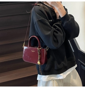 Detail van een bordeaux glanzende leren crossbodytas met gevlochten touwaccessoire