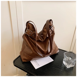 Detail of soft brown PU leather tote bag with metallic adjustable buckle on black table